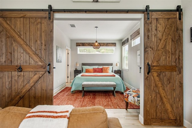 bedroom with a barn door, light wood-style floors, visible vents, and baseboards