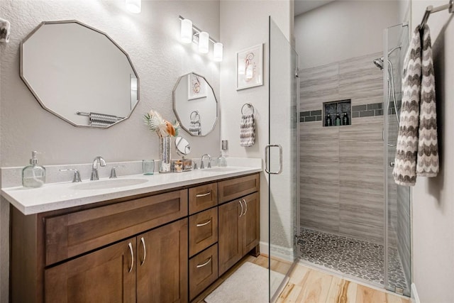 bathroom with double vanity, a sink, a stall shower, and wood finished floors