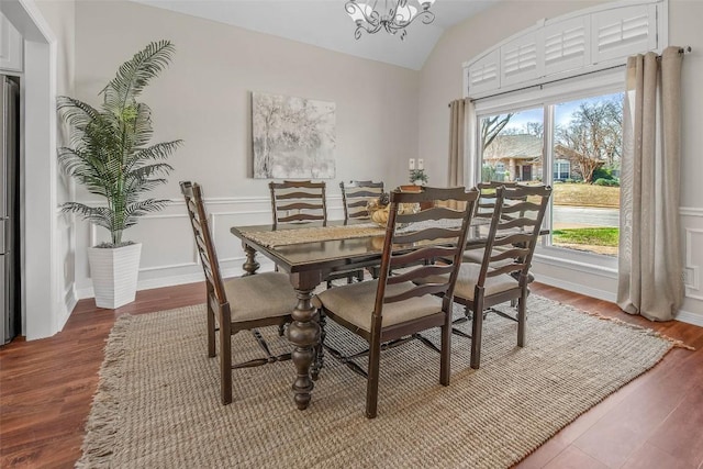 dining area featuring an inviting chandelier, lofted ceiling, wood finished floors, and a wainscoted wall