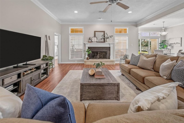 living room featuring a glass covered fireplace, ornamental molding, baseboards, and wood finished floors