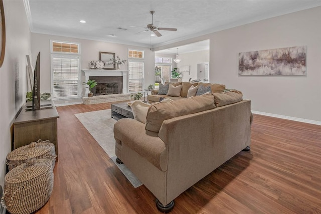 living area featuring ornamental molding, wood finished floors, baseboards, a brick fireplace, and ceiling fan