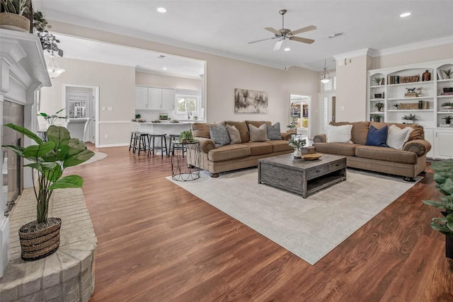 living area featuring visible vents, a ceiling fan, wood finished floors, recessed lighting, and crown molding