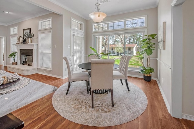 dining space with crown molding, a brick fireplace, wood finished floors, and baseboards