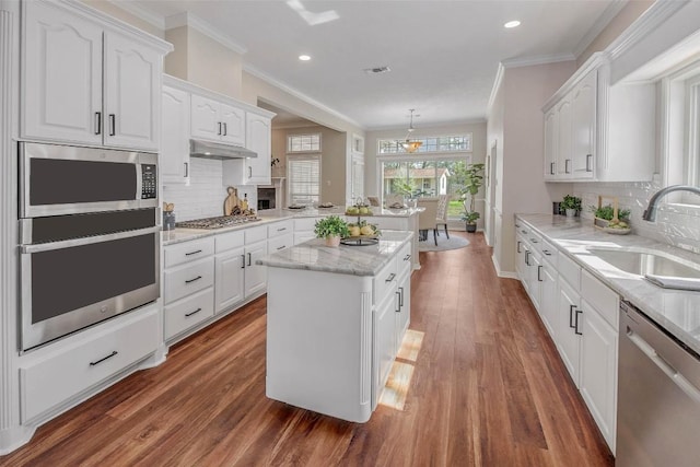 kitchen featuring a sink, under cabinet range hood, white cabinetry, stainless steel appliances, and a peninsula