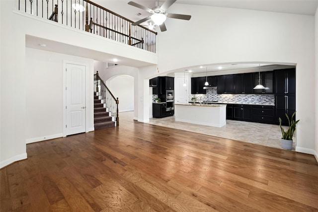 unfurnished living room featuring arched walkways, stairway, light wood-type flooring, and baseboards