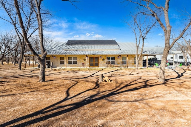 rear view of house with stone siding, roof mounted solar panels, and metal roof