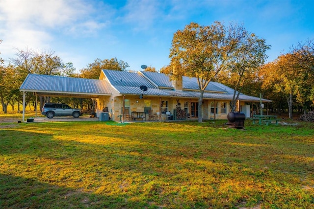 rear view of property with an attached carport, a lawn, metal roof, stone siding, and heating fuel