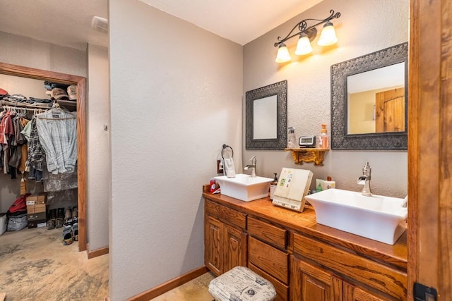 bathroom featuring double vanity, a spacious closet, baseboards, and a sink