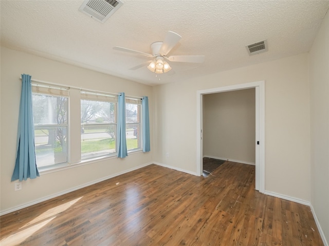 spare room with visible vents, a textured ceiling, baseboards, and wood finished floors