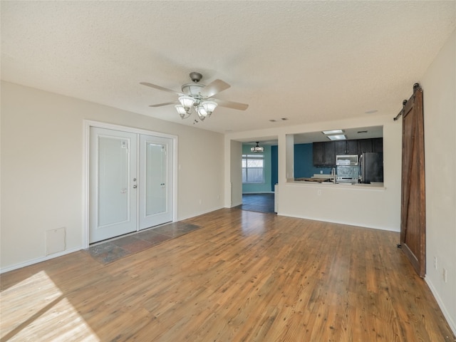 unfurnished living room with baseboards, a barn door, hardwood / wood-style flooring, a textured ceiling, and a ceiling fan