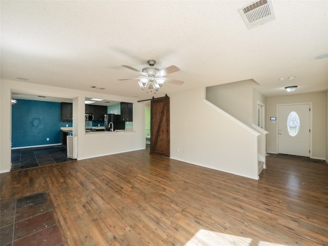 unfurnished living room with a barn door, visible vents, wood finished floors, and a ceiling fan