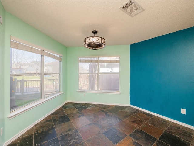 empty room with visible vents, baseboards, a textured ceiling, and stone tile flooring