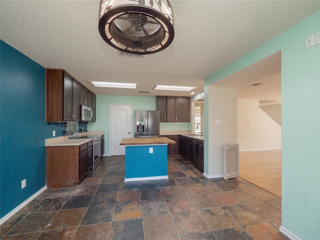 kitchen with dark brown cabinets, wooden counters, a kitchen island, appliances with stainless steel finishes, and a sink