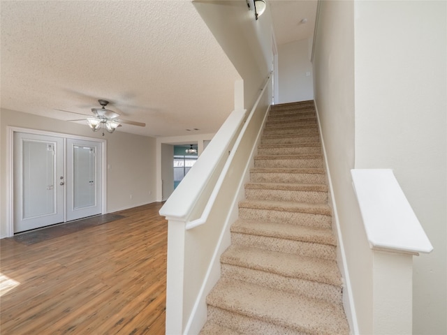 stairway with baseboards, a textured ceiling, a ceiling fan, and wood finished floors