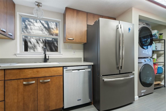 kitchen with brown cabinetry, stacked washer and clothes dryer, appliances with stainless steel finishes, and a sink