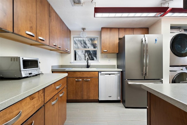 kitchen featuring visible vents, brown cabinets, a sink, appliances with stainless steel finishes, and stacked washer / dryer