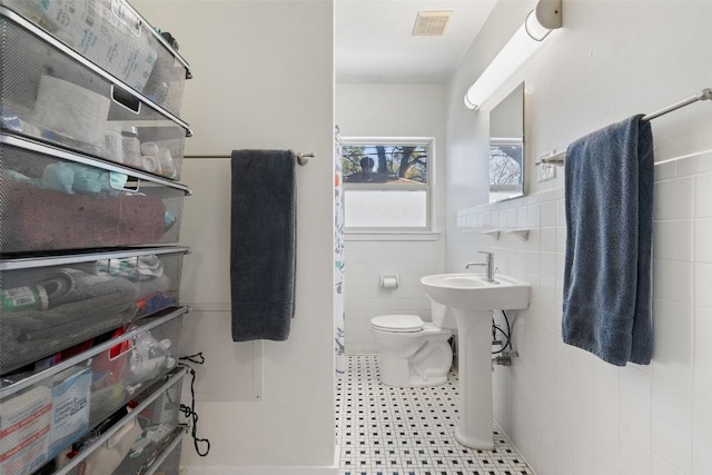 bathroom with visible vents, toilet, tile walls, and a wainscoted wall