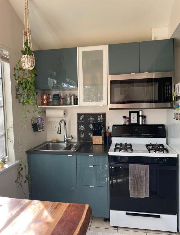 kitchen with a sink, stainless steel microwave, gas stove, light tile patterned floors, and lofted ceiling