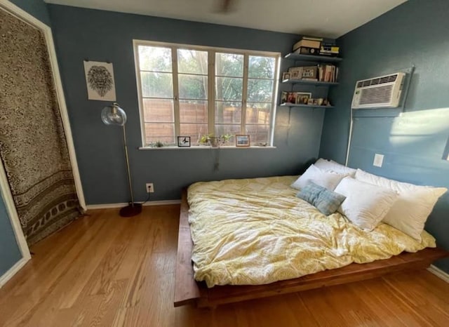 bedroom with an AC wall unit, baseboards, and wood finished floors