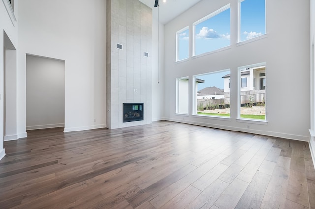 1821 Novara Trl, Leander, TX 78641 - unfurnished living room featuring a towering ceiling, dark wood-style floors, a tiled fireplace, and baseboards