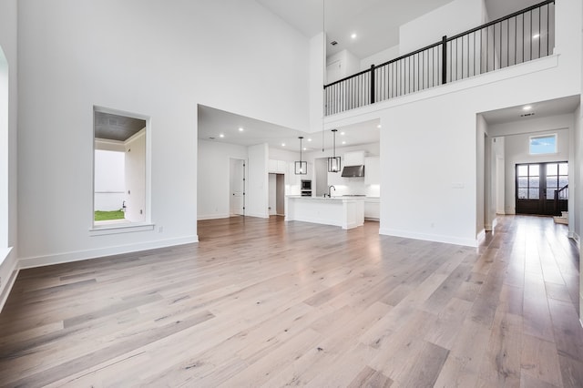 1821 Novara Trl, Leander, TX 78641 - unfurnished living room featuring light wood-style floors, a towering ceiling, a sink, and baseboards