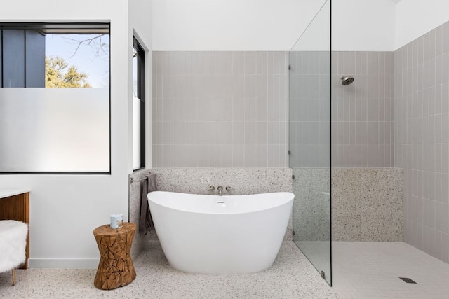 full bathroom featuring a freestanding tub, tile walls, speckled floor, and a walk in shower