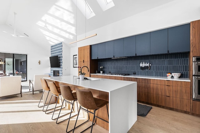 kitchen with tasteful backsplash, a breakfast bar, light countertops, light wood-style flooring, and a sink