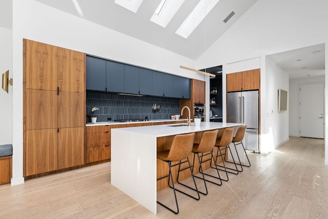 kitchen featuring light wood finished floors, a breakfast bar area, high quality fridge, modern cabinets, and a sink