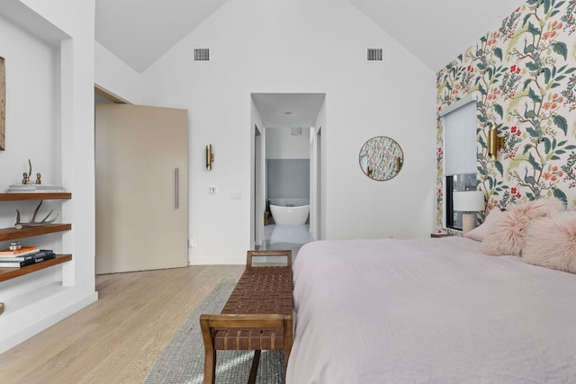 bedroom featuring ensuite bath, wood finished floors, visible vents, and high vaulted ceiling