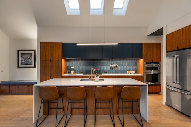 kitchen with light wood finished floors, a sink, appliances with stainless steel finishes, brown cabinets, and backsplash