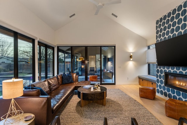 living room with visible vents, wood finished floors, a ceiling fan, and a glass covered fireplace