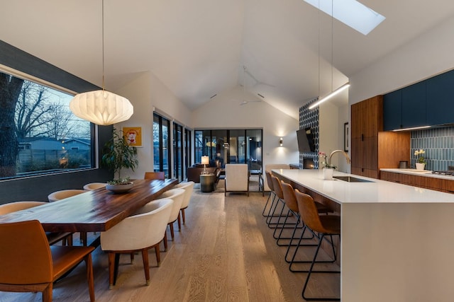 dining area featuring a skylight, light wood-type flooring, and high vaulted ceiling