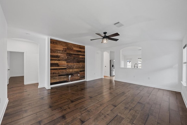 unfurnished living room with an accent wall, dark wood-style floors, visible vents, and arched walkways