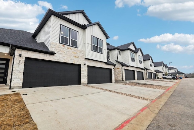 view of front of property featuring driveway, an attached garage, stone siding, board and batten siding, and a residential view