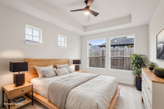 bedroom with light colored carpet, a ceiling fan, a raised ceiling, and baseboards