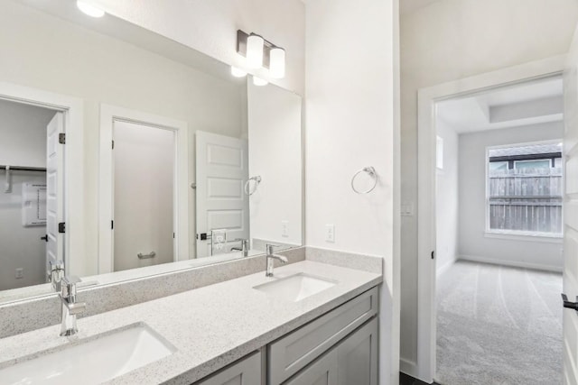 full bathroom with double vanity, a tray ceiling, baseboards, and a sink