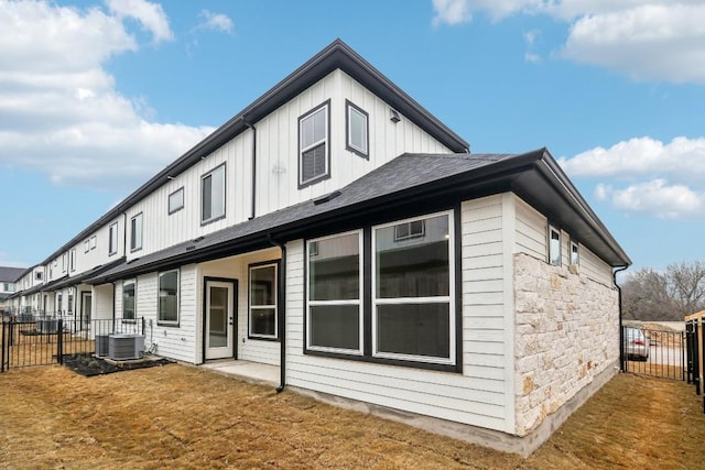 rear view of house featuring board and batten siding, fence, central AC unit, a lawn, and stone siding