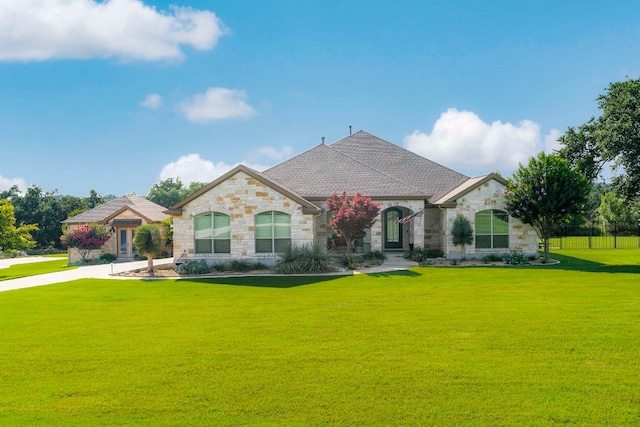 french country home featuring stone siding, a front yard, and a shingled roof