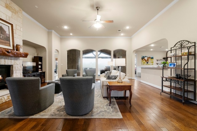 living room with crown molding, baseboards, hardwood / wood-style floors, a fireplace, and arched walkways