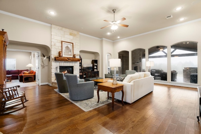 living area featuring ornamental molding, a ceiling fan, dark wood finished floors, recessed lighting, and a stone fireplace