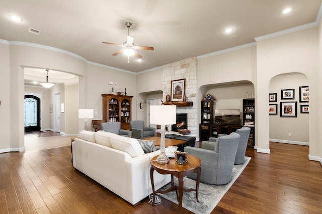 living room with dark wood finished floors, a stone fireplace, crown molding, and baseboards