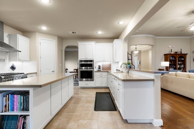 kitchen with visible vents, a sink, arched walkways, double oven, and wall chimney exhaust hood