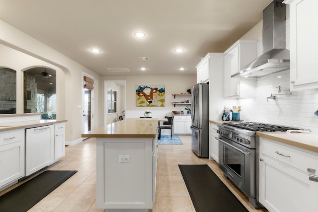 kitchen with a kitchen island, appliances with stainless steel finishes, white cabinetry, wall chimney range hood, and backsplash