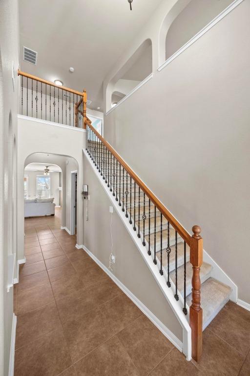 stairs with visible vents, arched walkways, tile patterned flooring, baseboards, and a towering ceiling