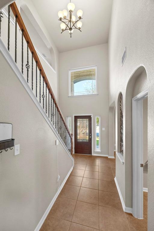 foyer entrance featuring visible vents, a high ceiling, tile patterned flooring, stairs, and a chandelier