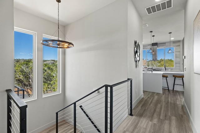 hall with wood finished floors, an upstairs landing, visible vents, and baseboards