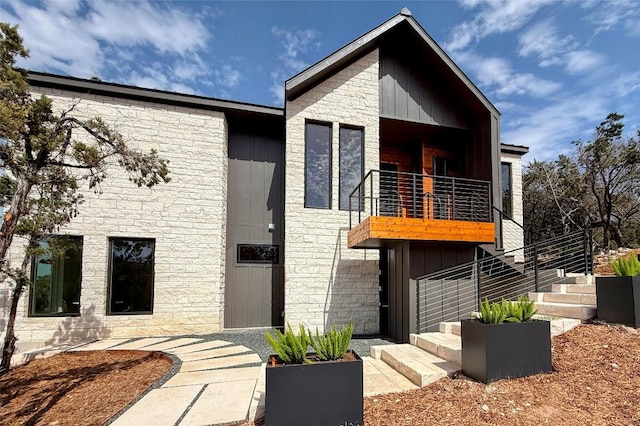 modern home with a balcony, board and batten siding, and stone siding