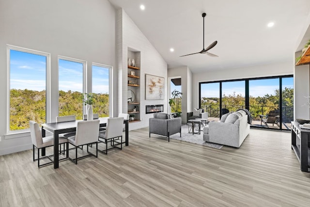 dining room with a healthy amount of sunlight, a fireplace, a ceiling fan, and light wood-style floors