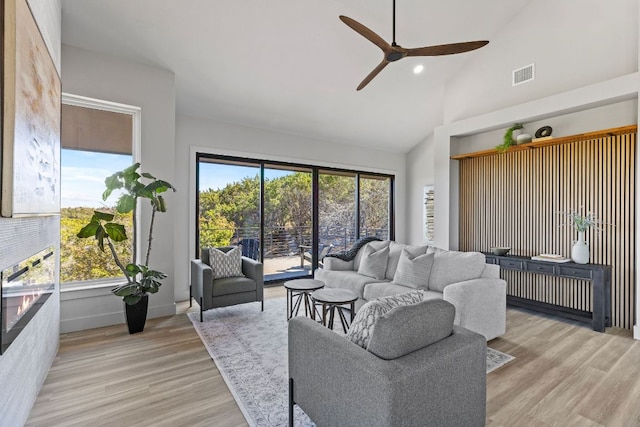 living room featuring visible vents, baseboards, ceiling fan, light wood-style floors, and high vaulted ceiling