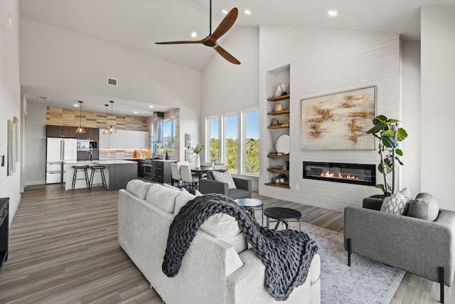 living room featuring visible vents, wood finished floors, high vaulted ceiling, and a glass covered fireplace